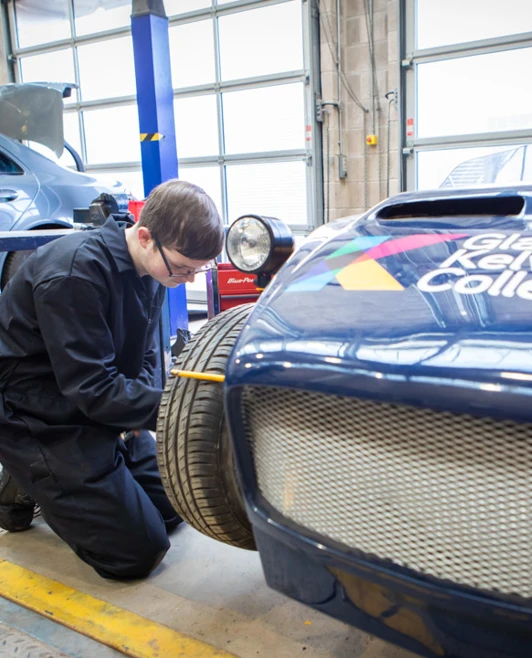 Student working on the front wheel of a Glasgow Kelvin College-branded kit car, checking its alignment and assembly. Student working on the front wheel of a Glasgow Kelvin College-branded kit car, checking its alignment and assembly.